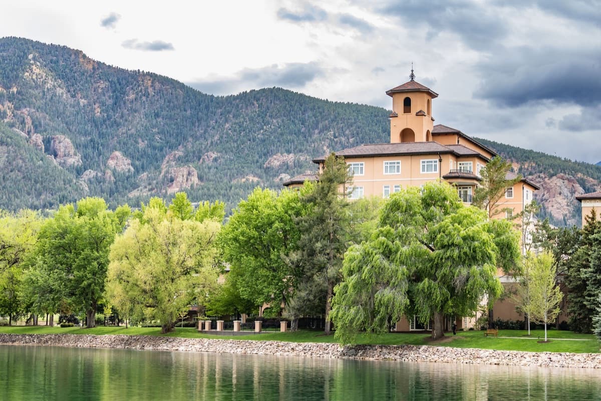 The Broadmoor's tower rising over Cheyenne Lake, willows along the shoreline, Cheyenne Mountain behind
